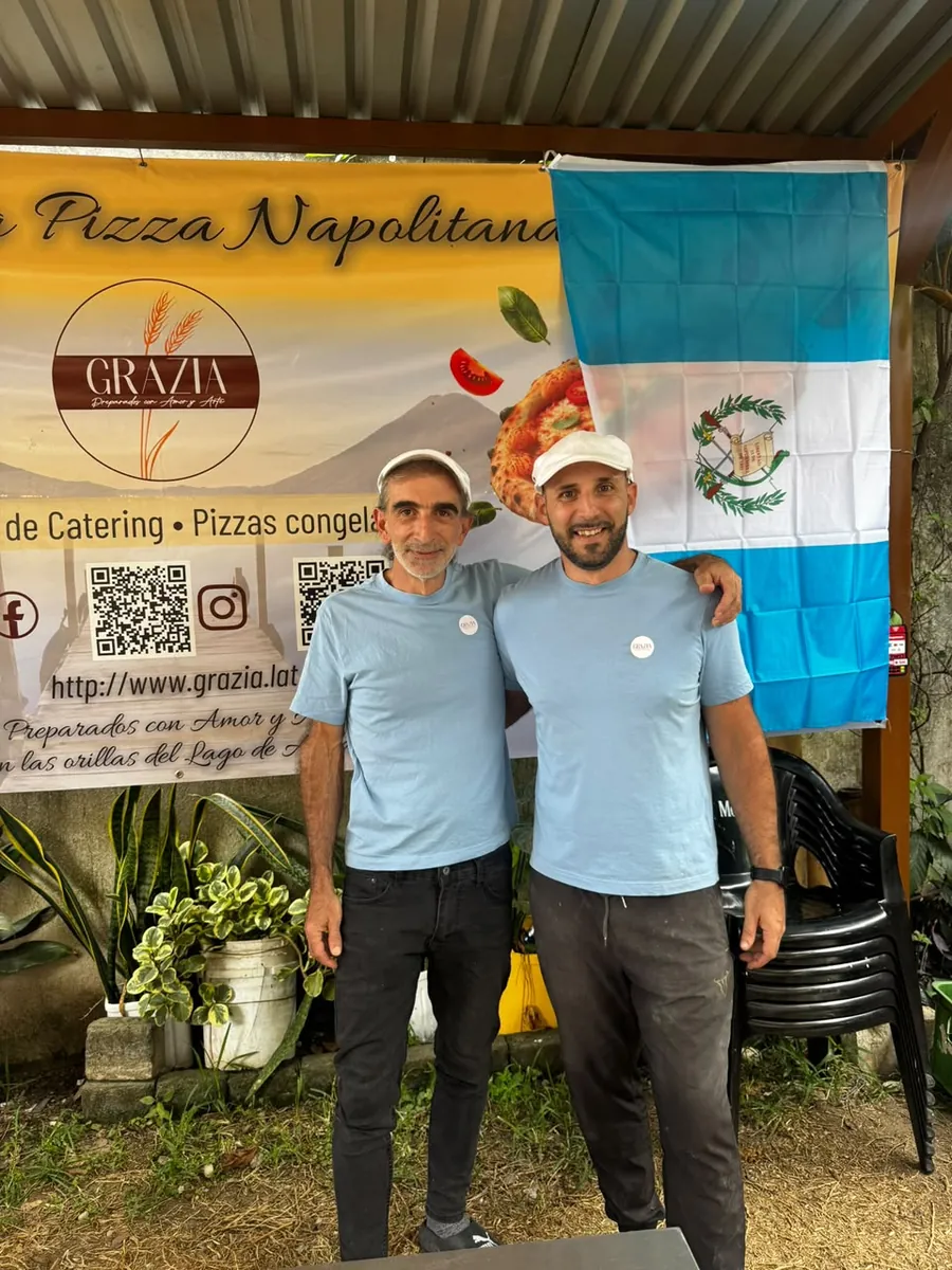 The two Italians behind Grazia in the house T-shirt, in front of the restaurant banner and the Guatemalan flag in Panajachel